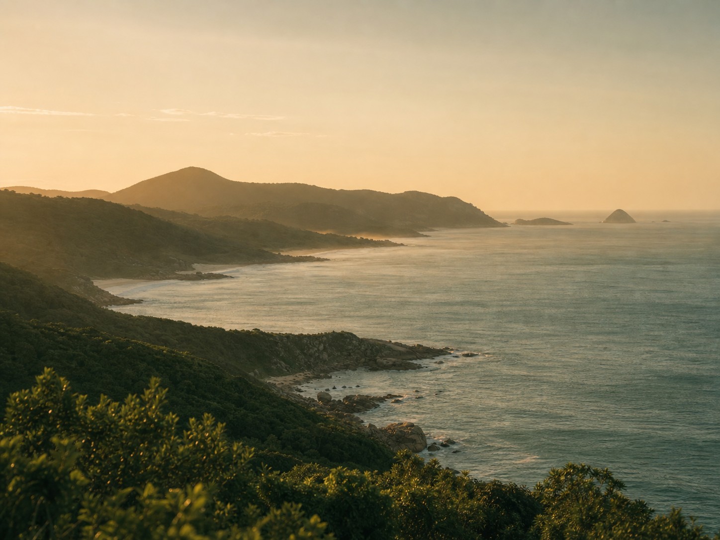 Vista costeira do Sul da Ilha de Florianópolis com morros verdes e mar ao entardecer